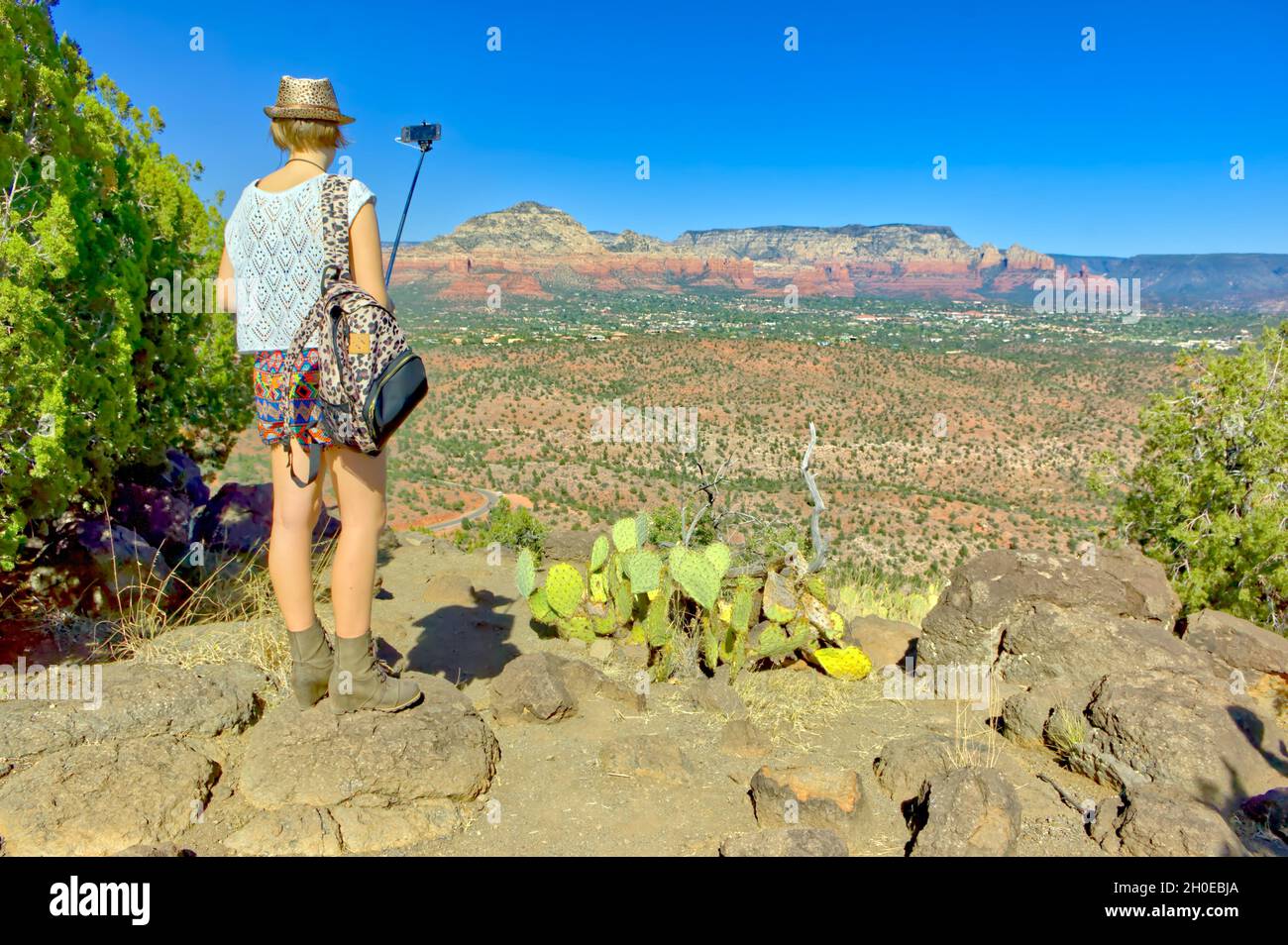 A young woman taking a cell phone photo of the Sedona landscape in Arizona like other typical tourists. In the background is Thunder Mountain and Coff Stock Photo