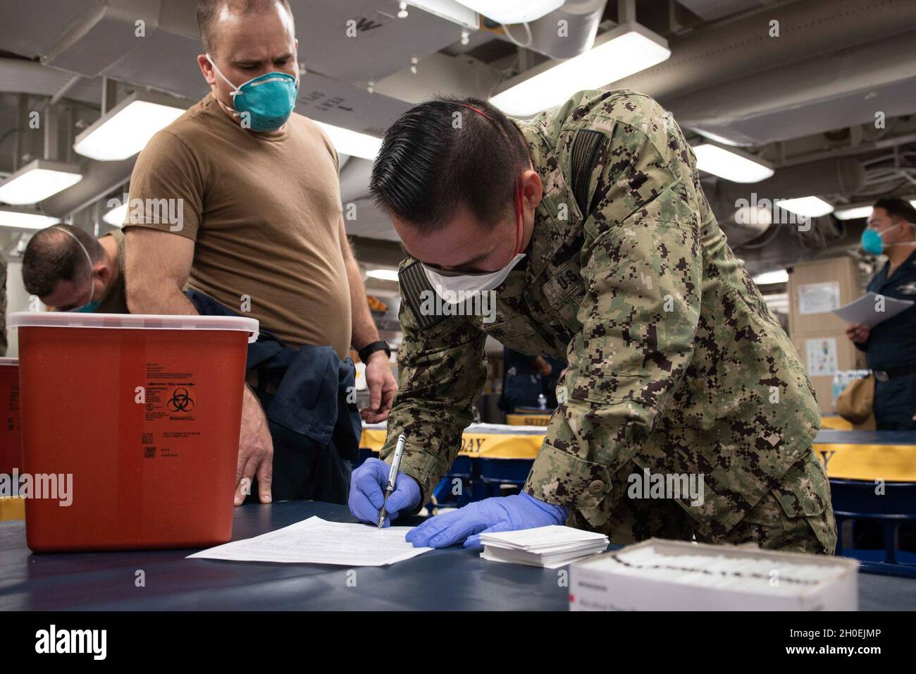 210213-N-QD512-1015 NORFOLK, Va. (Feb. 13, 2020) Hospital Corpsman 1st Class Thai Dinh, from El Monte, California, right, prepares paperwork before administering a COVID-19 vaccine to Cmdr. Thomas McCandless, commanding officer of the Arleigh-Burke class guided-missile destroyer USS Mitscher (DDG 57). Mitscher is currently pier side conducting routine maintenance. Stock Photo