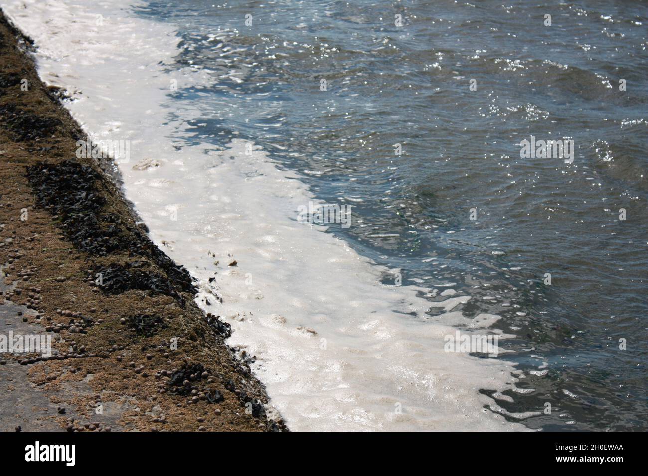 A wave with sea foam crashes upon the coast of Scotland. Stock Photo