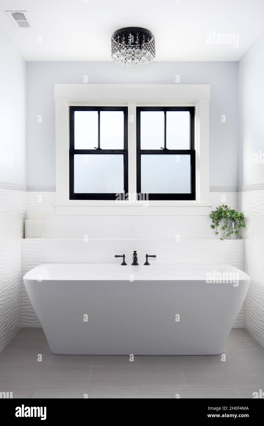 A beautiful, luxury bathroom with a light hanging above a white Fleurco  standalone tub and black faucet surrounded by tiles Stock Photo - Alamy
