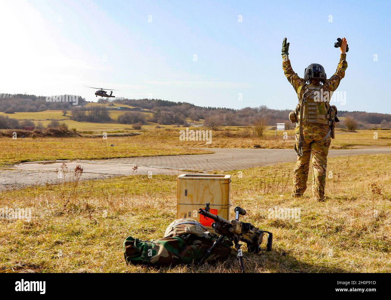U.S. Army Staff Sgt. Vanessa Goggia, a crew chief with Alpha Company, 1st Battalion, 214th Aviation Regiment, delivers a hand and arm signal to a UH-60 Black Hawk after completing a ground firing table with the 240B machine gun Feb. 23, 2021, at Baumholder Training Area, Baumholder, Germany, as part of Cougar Flurry, the battalion's training exercise. Stock Photo