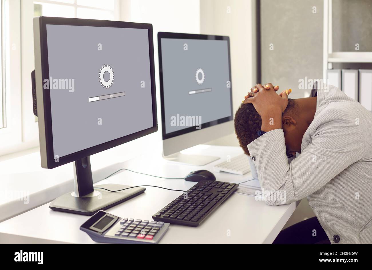 Woman sitting in front of office computers and waiting for software update to install Stock Photo