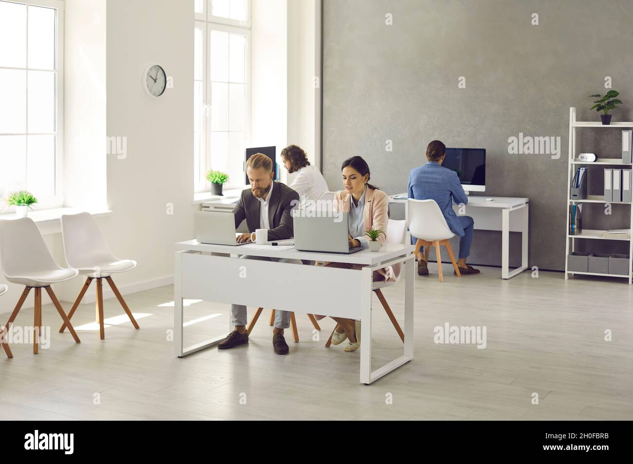 Modern interior of company's workplace with employees sitting at tables with laptops. Stock Photo