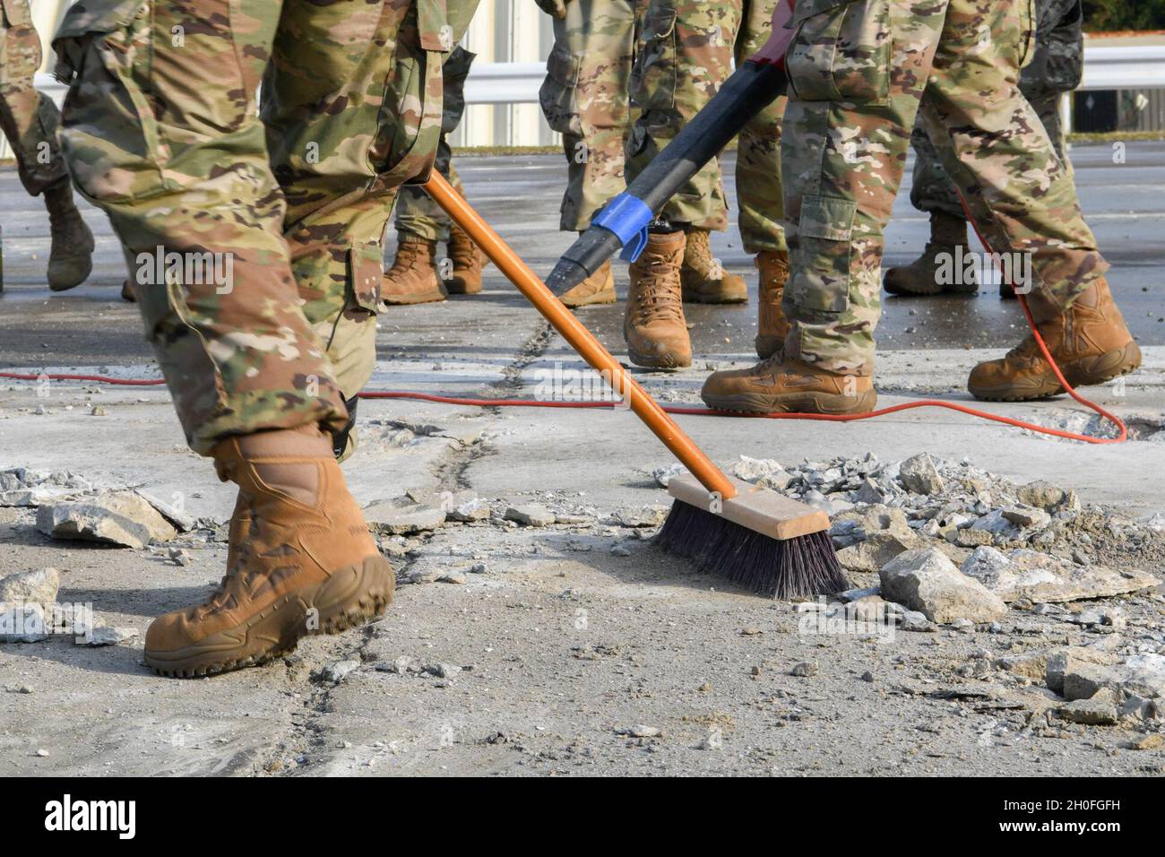 U.S. Air Force Airmen from the 18th Wing clear chips of cement, called spall, from a hole in an airfield during a Multi-Capable Airmen course exercise at Kadena Air Base, Japan, Feb. 25, 2021. Clearing the hole of debris is step one of expedient spall repair, a multi-staged process that allows use of an airfield to be quickly reestablished in the event of high-impact damage. In terms of scale, a hole five feet wide is considered a spall, anything bigger is considered a crater. Stock Photo