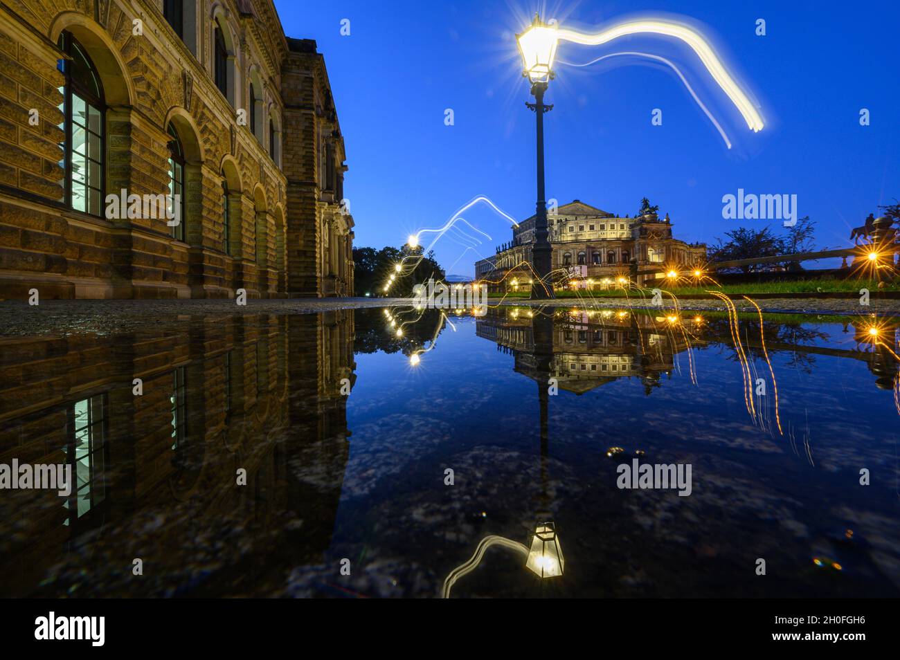 Dresden, Germany. 12th Oct, 2021. The Zwinger (l) and the Semperoper Schinkelwache are reflected in a puddle on Theaterplatz in the evening after a rain shower. (Shot with motion effect). Credit: Robert Michael/dpa-Zentralbild/dpa/Alamy Live News Stock Photo