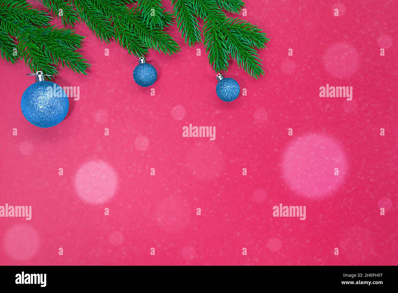 Spruce branches with blue Christmas tree shiny toys on pink background with snow bokeh. Copy space Stock Photo
