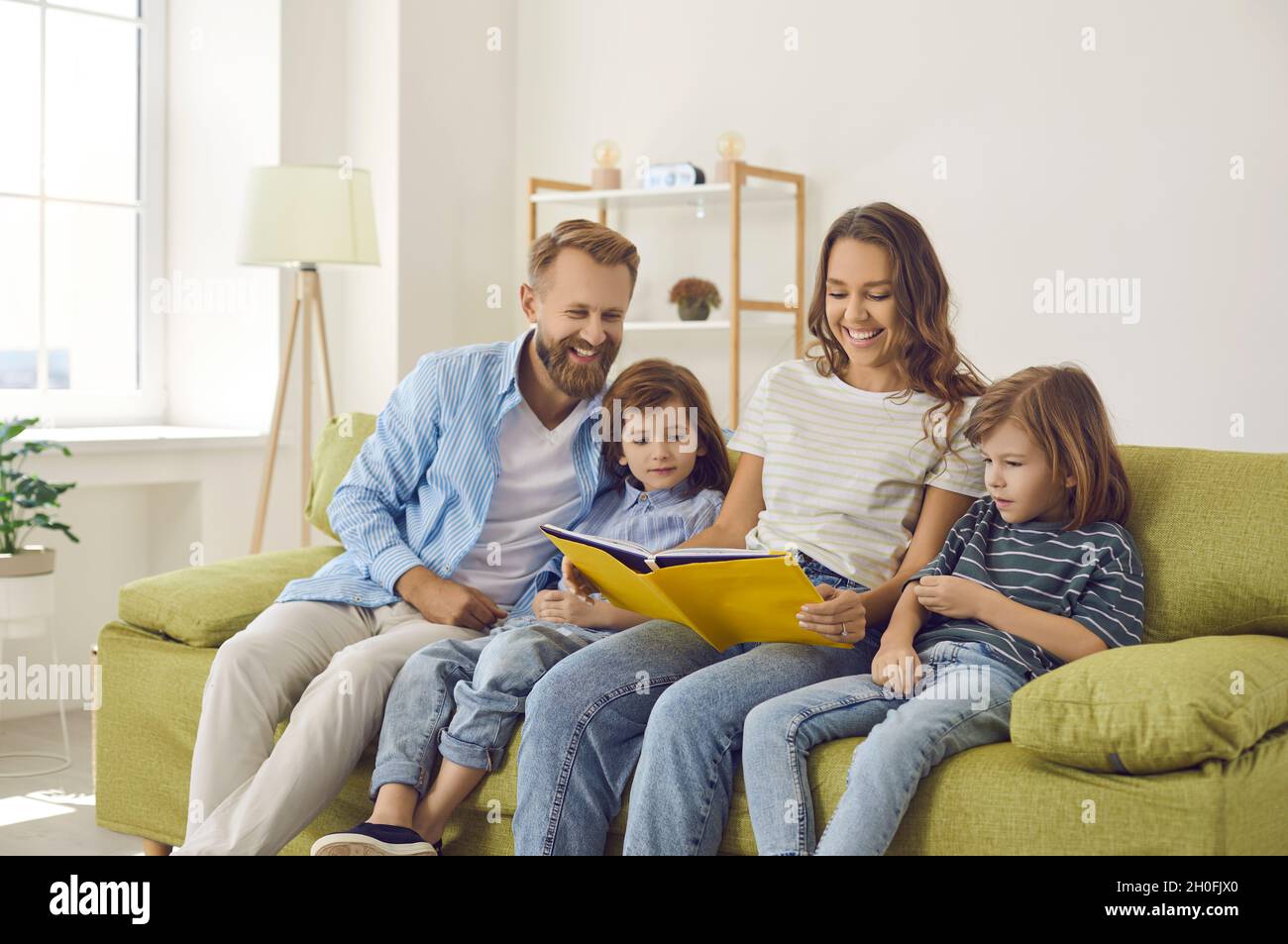 Happy mom, dad and kids looking through their family photo album or reading a book Stock Photo