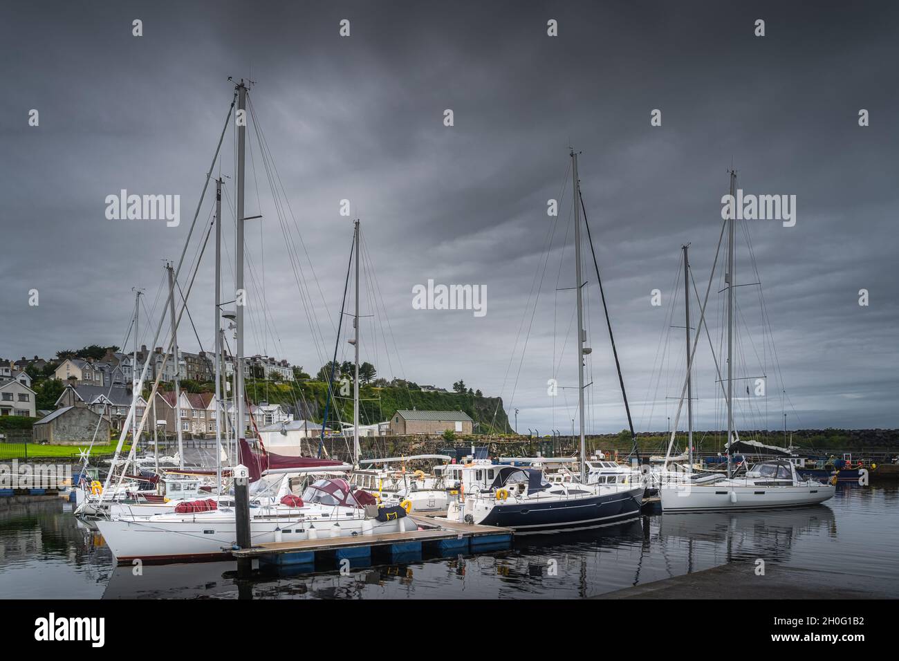 Yachts and sailboats moored in small, beautiful marina in Ballycastle town with dark storm clouds, Antrim, Northern Ireland Stock Photo