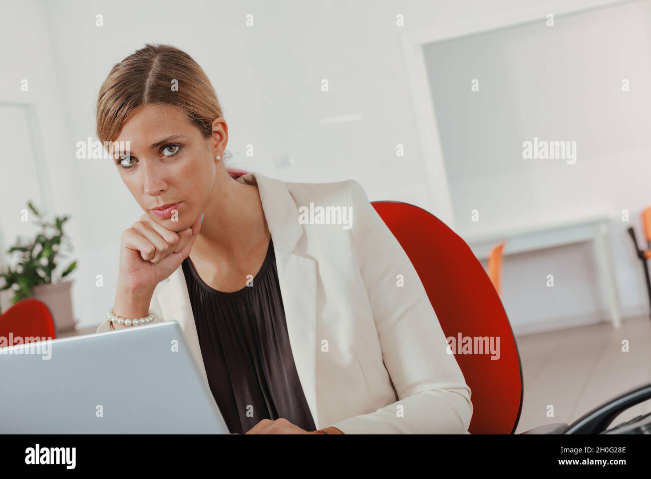 Businesswoman looking thoughtfully at camera with chin on hand as she sits  working ona laptop computer at her desk in the office Stock Photo - Alamy