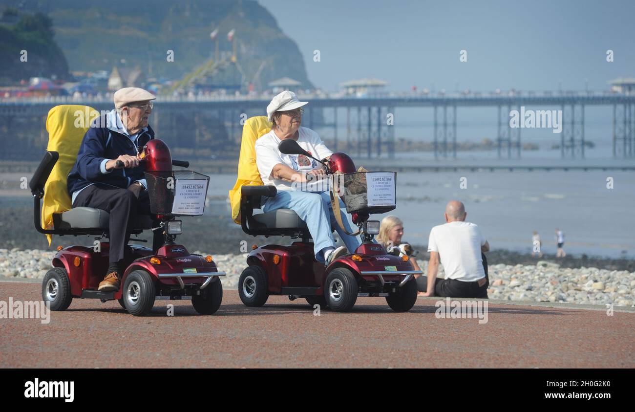 ELDERLY PEOPLE RIDING MOBILITY SCOOTERS ON THE SEAFRONT OF LLANDUDNO WALES UK RE RETIREMENT GOLDEN YEARS HOLIDAYS  MARRIAGE COUPLES ETC Stock Photo