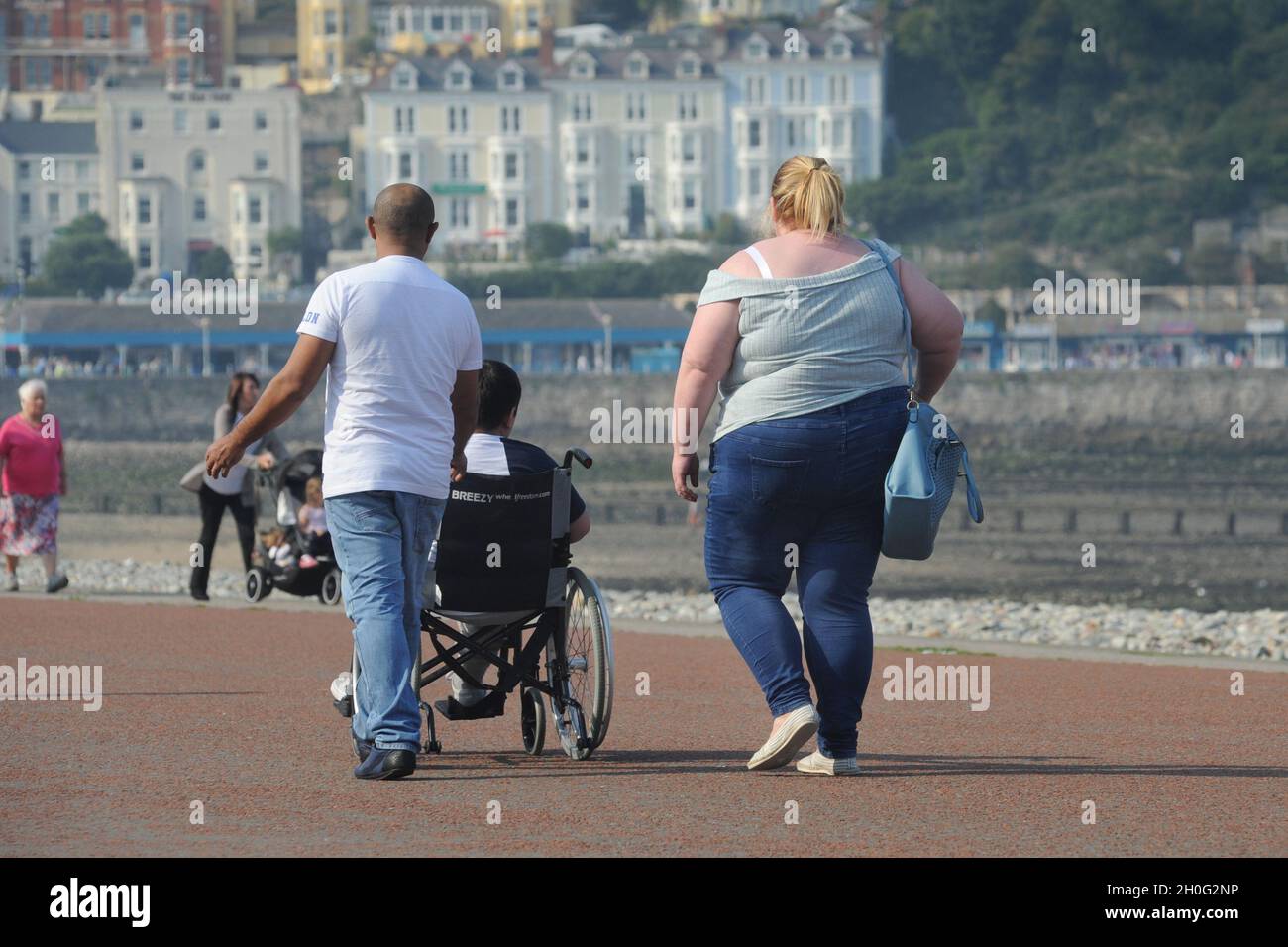 OVERWEIGHT PERSON WALKING ON THE SEAFRONT OF LLANDUDNO WALES UK RE OBESITY EXERCISE FOOD ETC Stock Photo