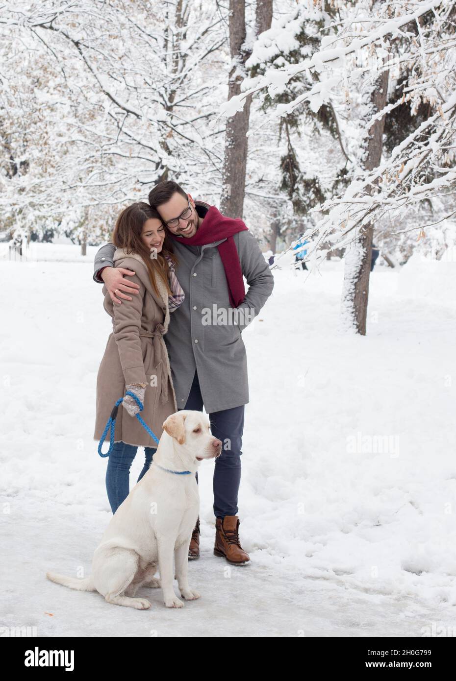 Young couple walking dog in park in winter time with lot of snow Stock Photo