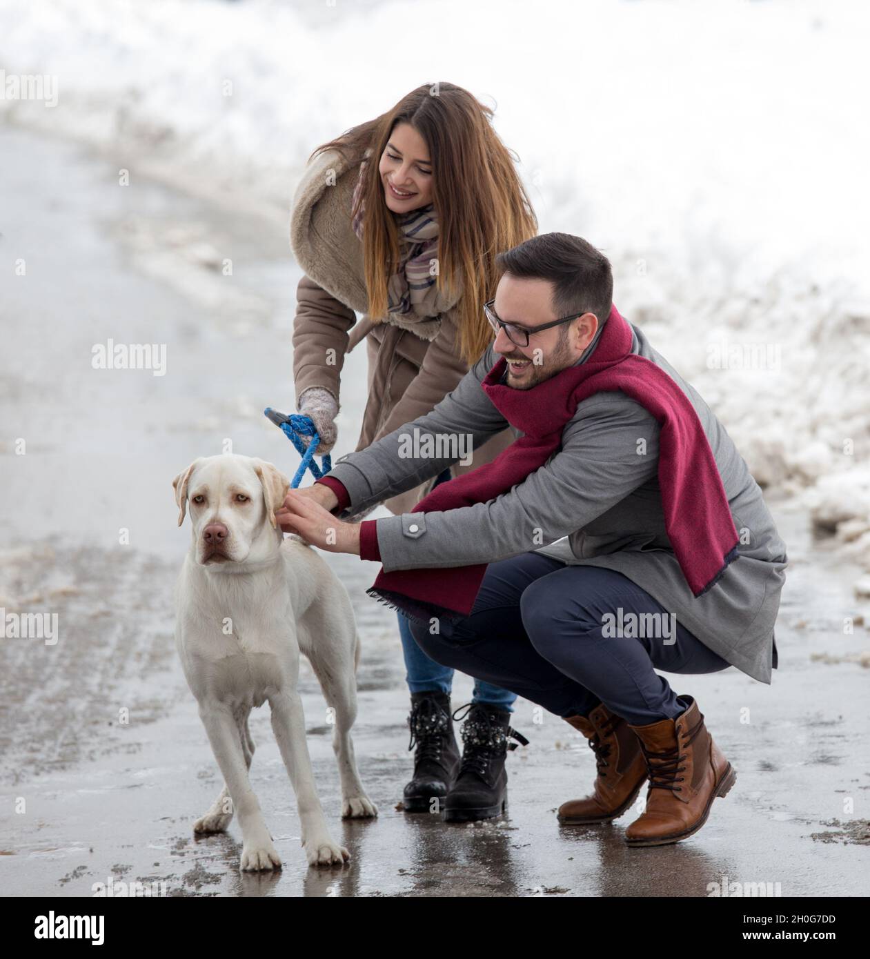 Young couple walking dog in park in winter time with lot of snow Stock Photo