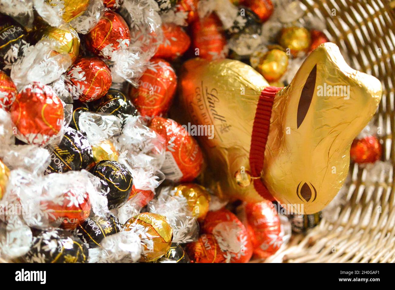 The iconic Lindt Chocolate Bunny wrapped in gold foil with distinctive red collar and bell, in a wicker Easter basket with eggs and Lindor chocolates Stock Photo