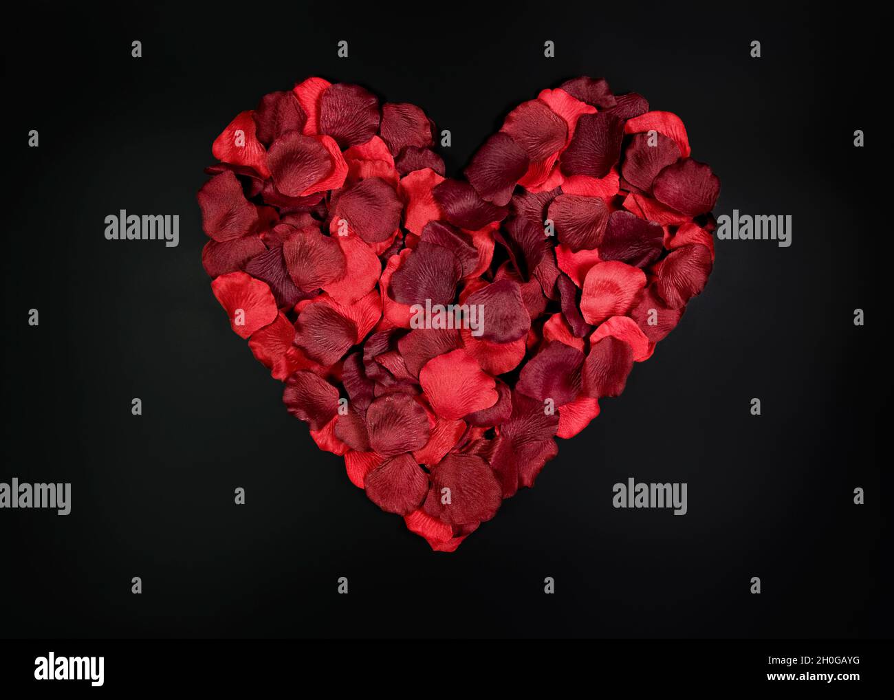 Red petals shaped into a heart on plain black background representing love and romance Stock Photo
