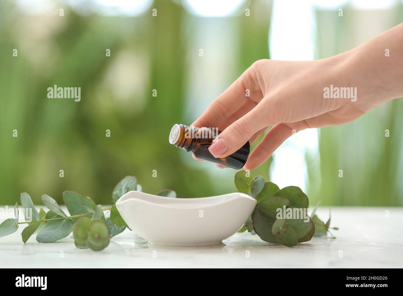 Woman adding essential oil to water in bowl on table Stock Photo - Alamy