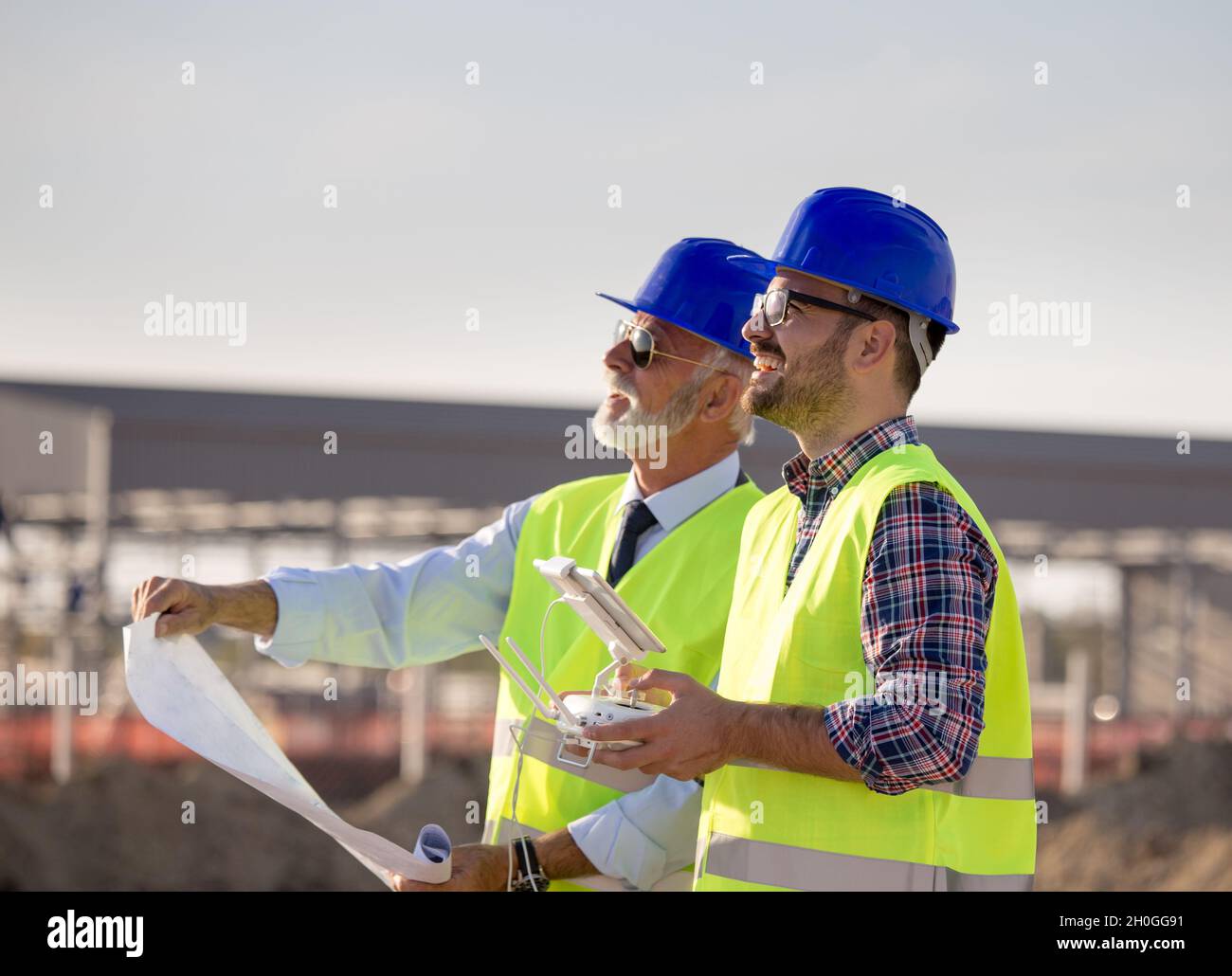 Two engineers with helmets and vests operating with drone by remote ...