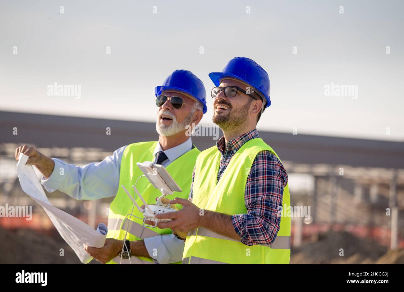 Two engineers with helmets and vests operating with drone by remote ...