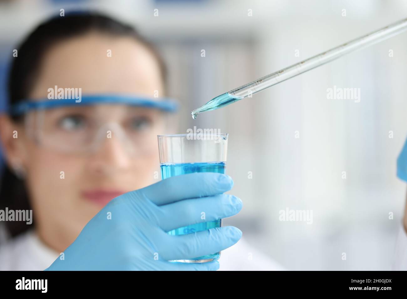 Female scientist dripping and pipetting into flask of blue liquid Stock Photo