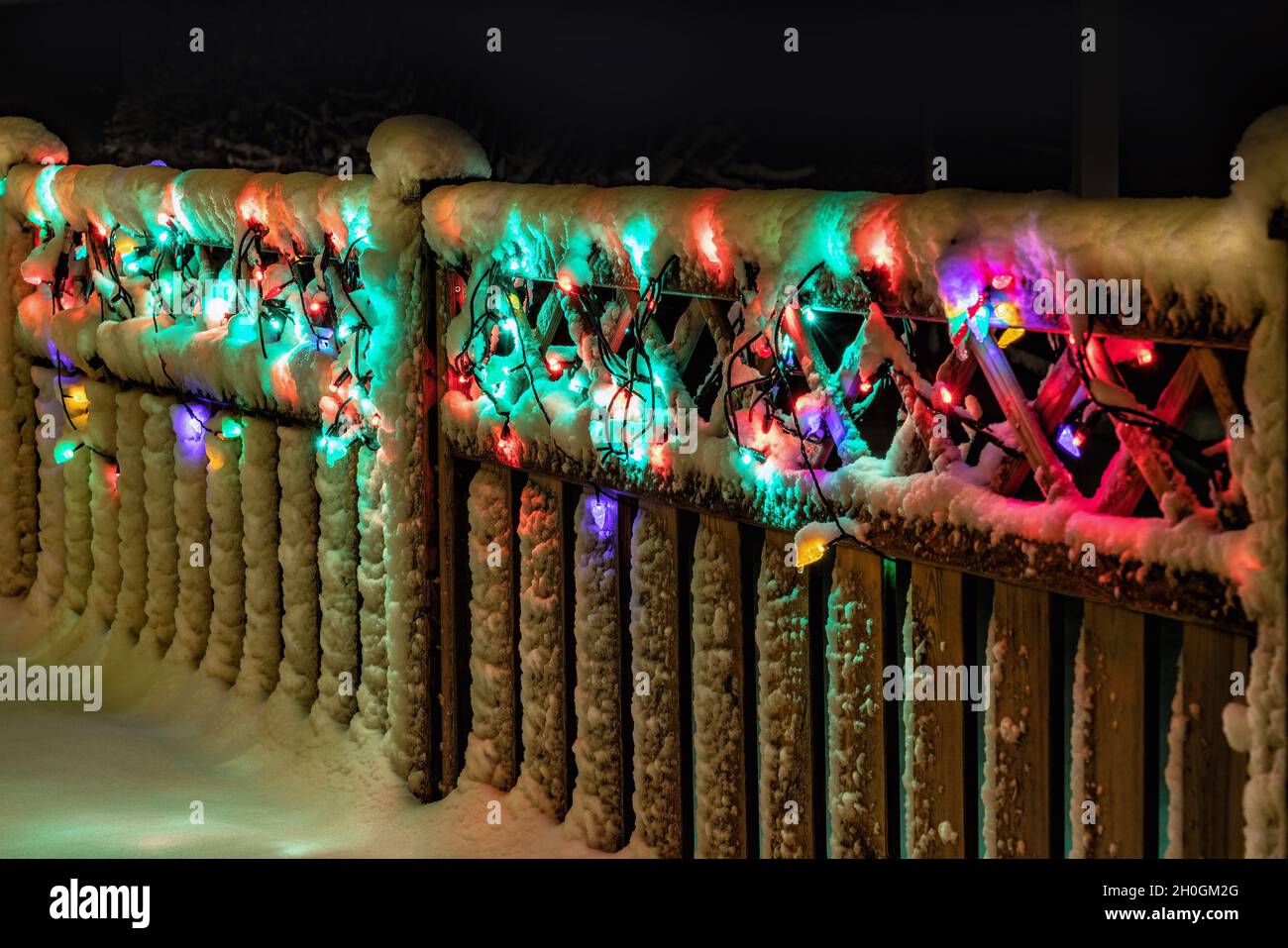 Christmas light decoration under snow on wooden fence, multicolored lights glowing, perspective view Stock Photo