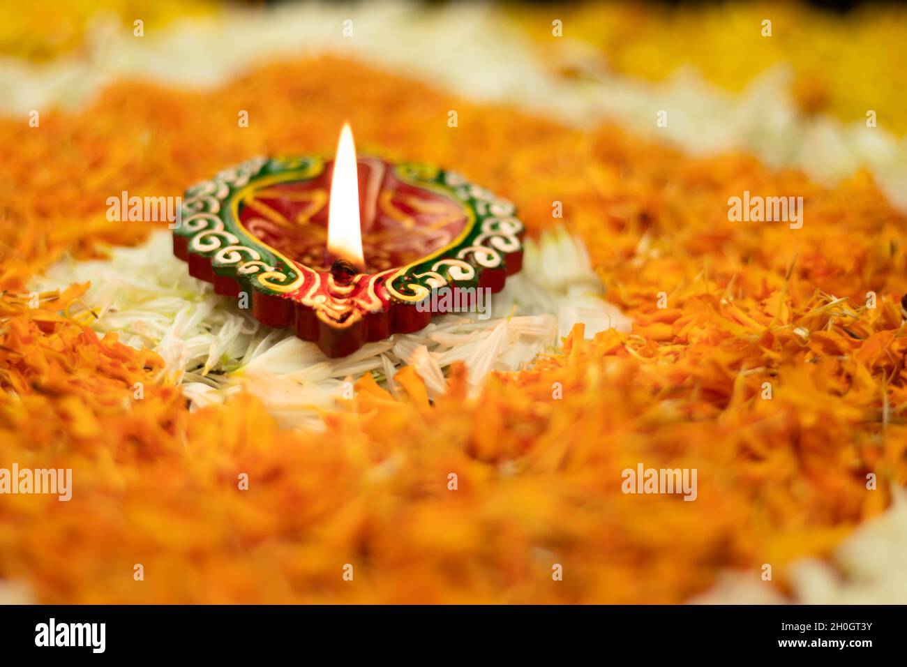 Handcrafted Clay Diya Lit On Floral Rangoli Made Of Marigold Flowers With Bokeh In Background. Indian Festival Theme For Diwali Pooja, Navratri Stock Photo