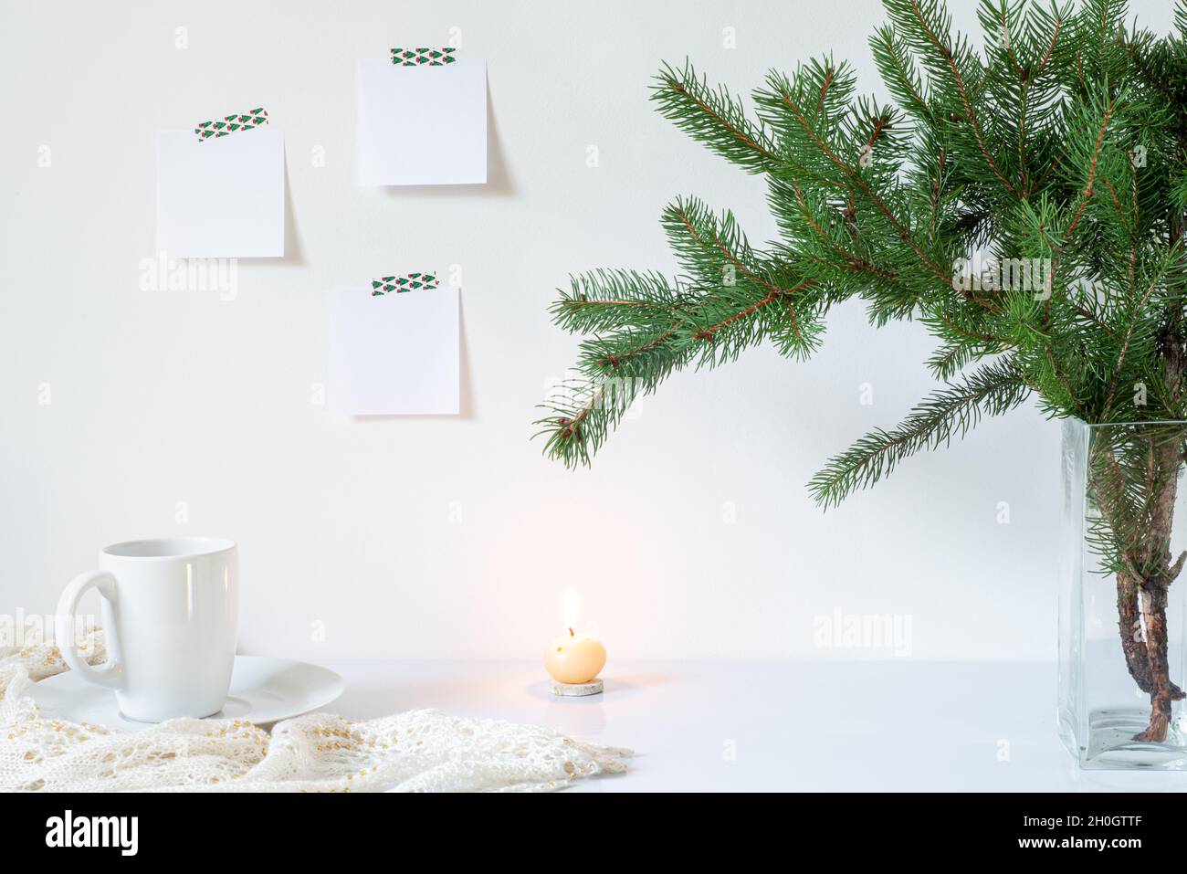 Festive breakfast still life.Cup of coffee, candle and vase with fir branches.Empty notepads mockup hanging on the white wall.Christmas decor.Working Stock Photo