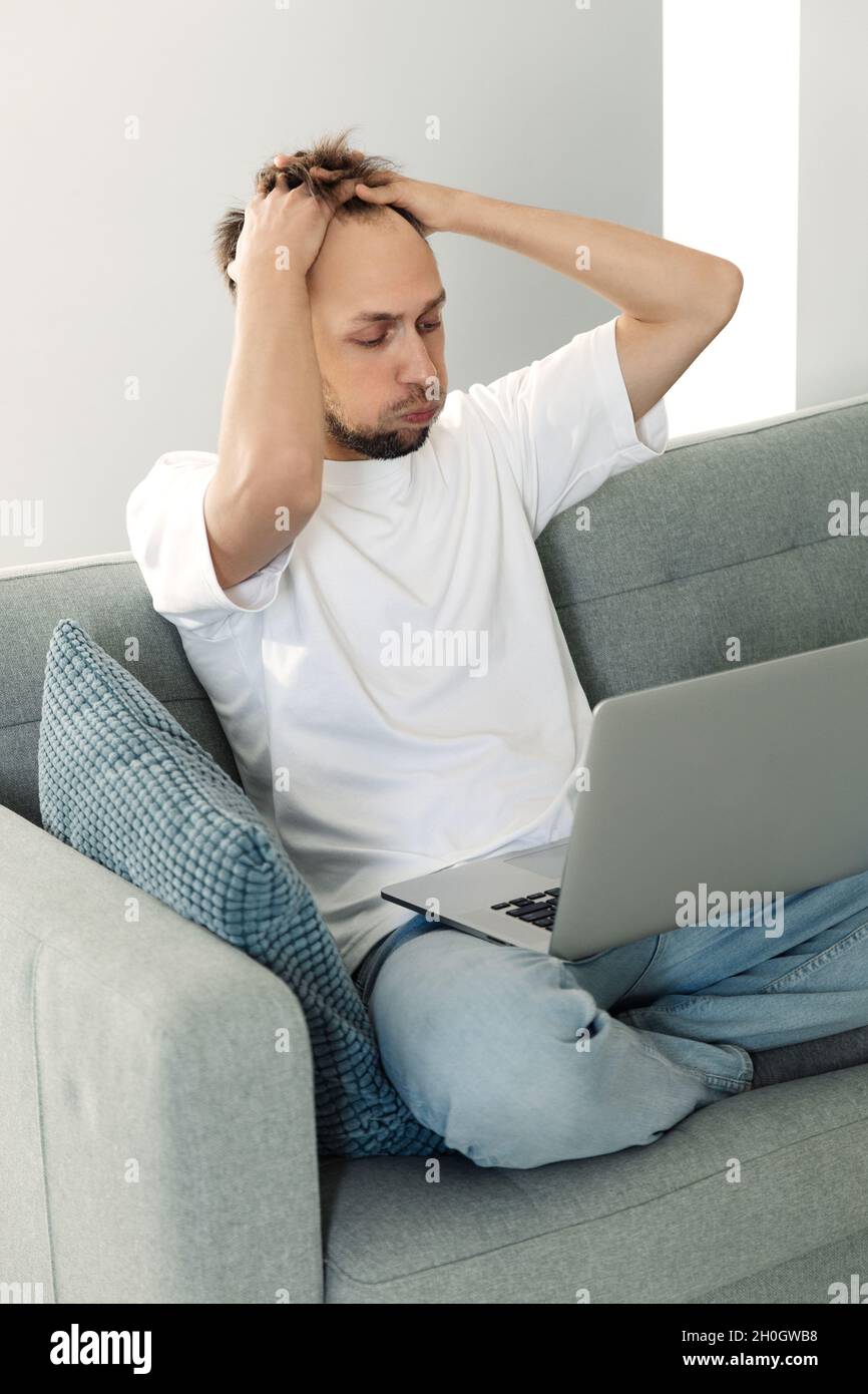 Suffering stress at work: tired remote worker man look at laptop frustrated with financial failure Stock Photo