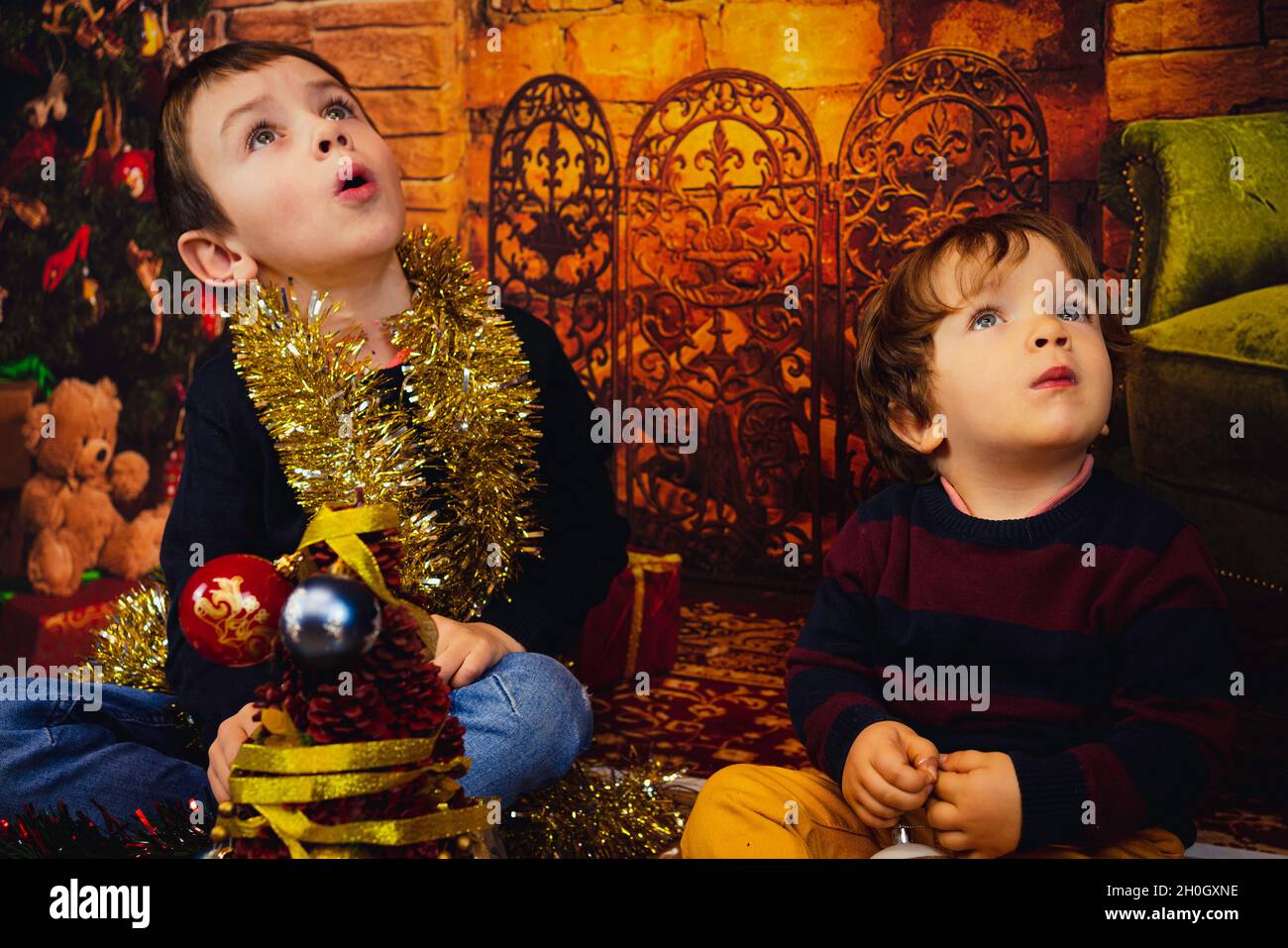 Two surprised baby boys sitting near a Christmas tree surrounded by Christmas decorations, Spain Stock Photo