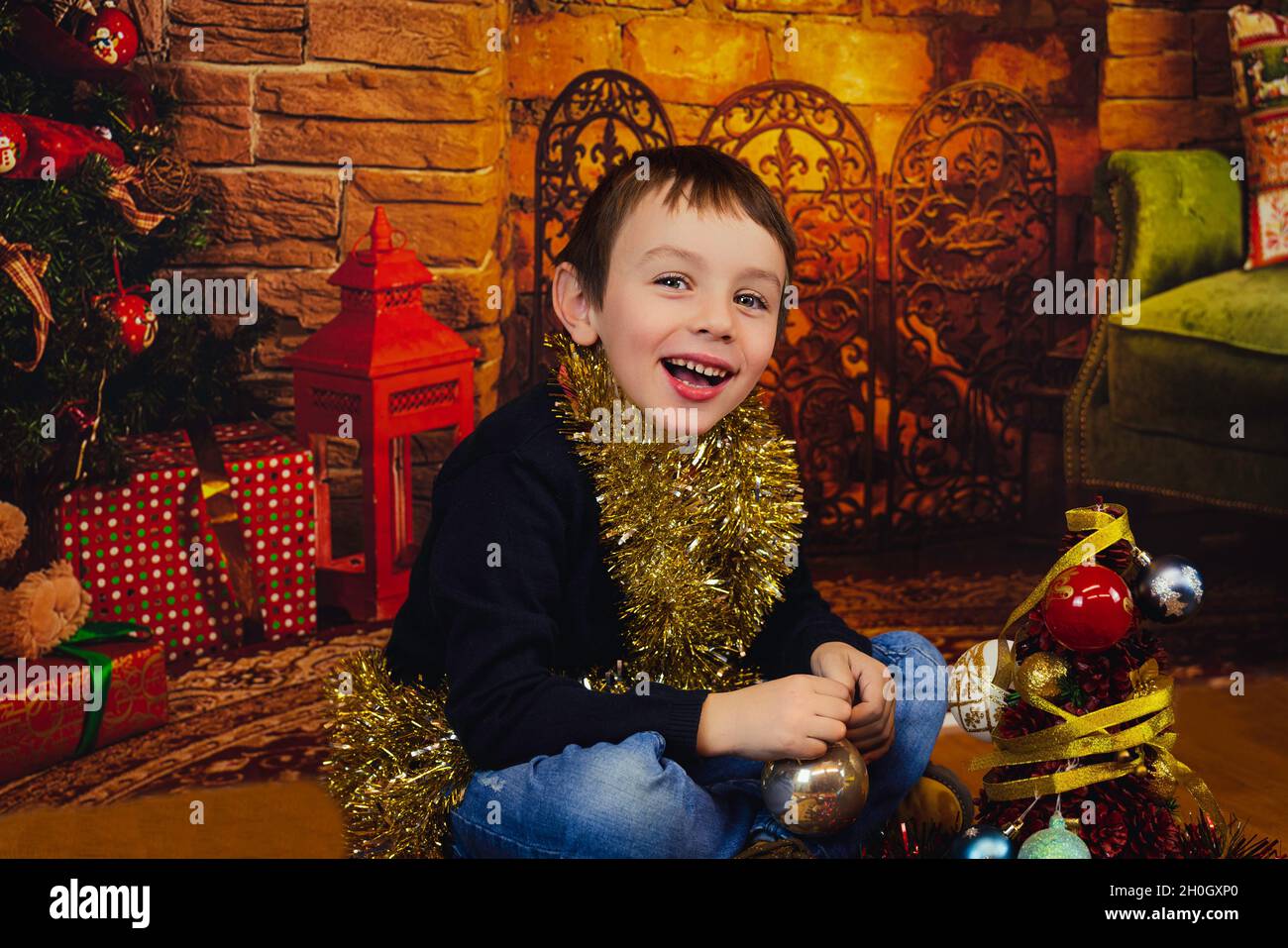 Cute, happy baby boy sitting near a Christmas tree wrapped with glossy tape, Spain Stock Photo