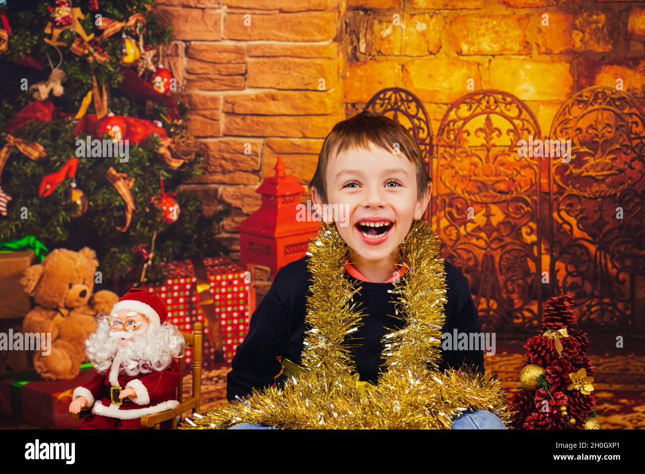 Cute, happy baby boy sitting near a Christmas tree wrapped with glossy tape, Spain Stock Photo