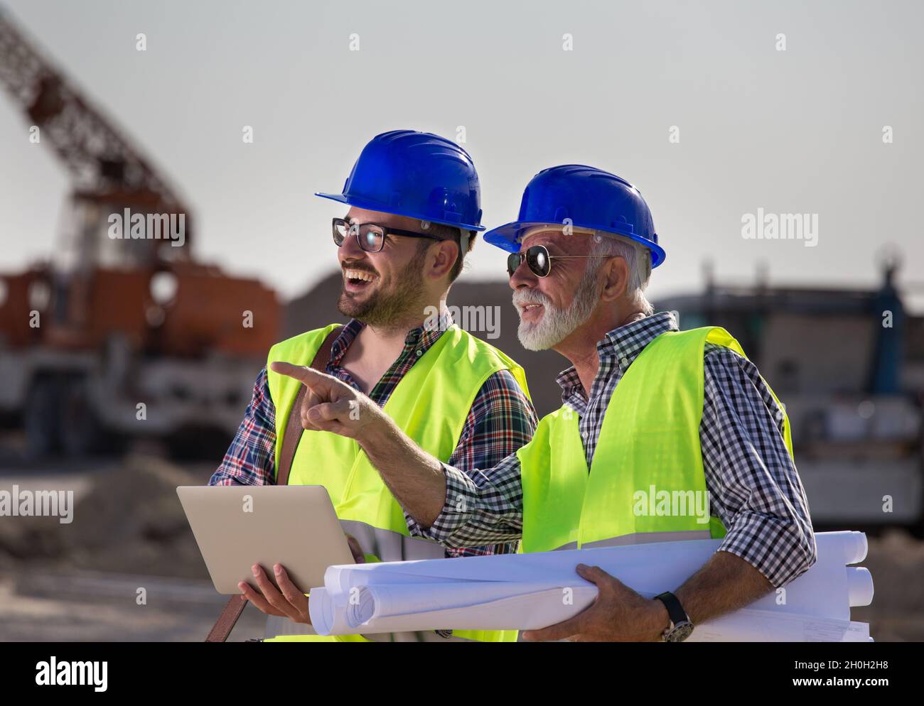 Twp satisfied engineers talking at building site with construction machinery in background Stock Photo