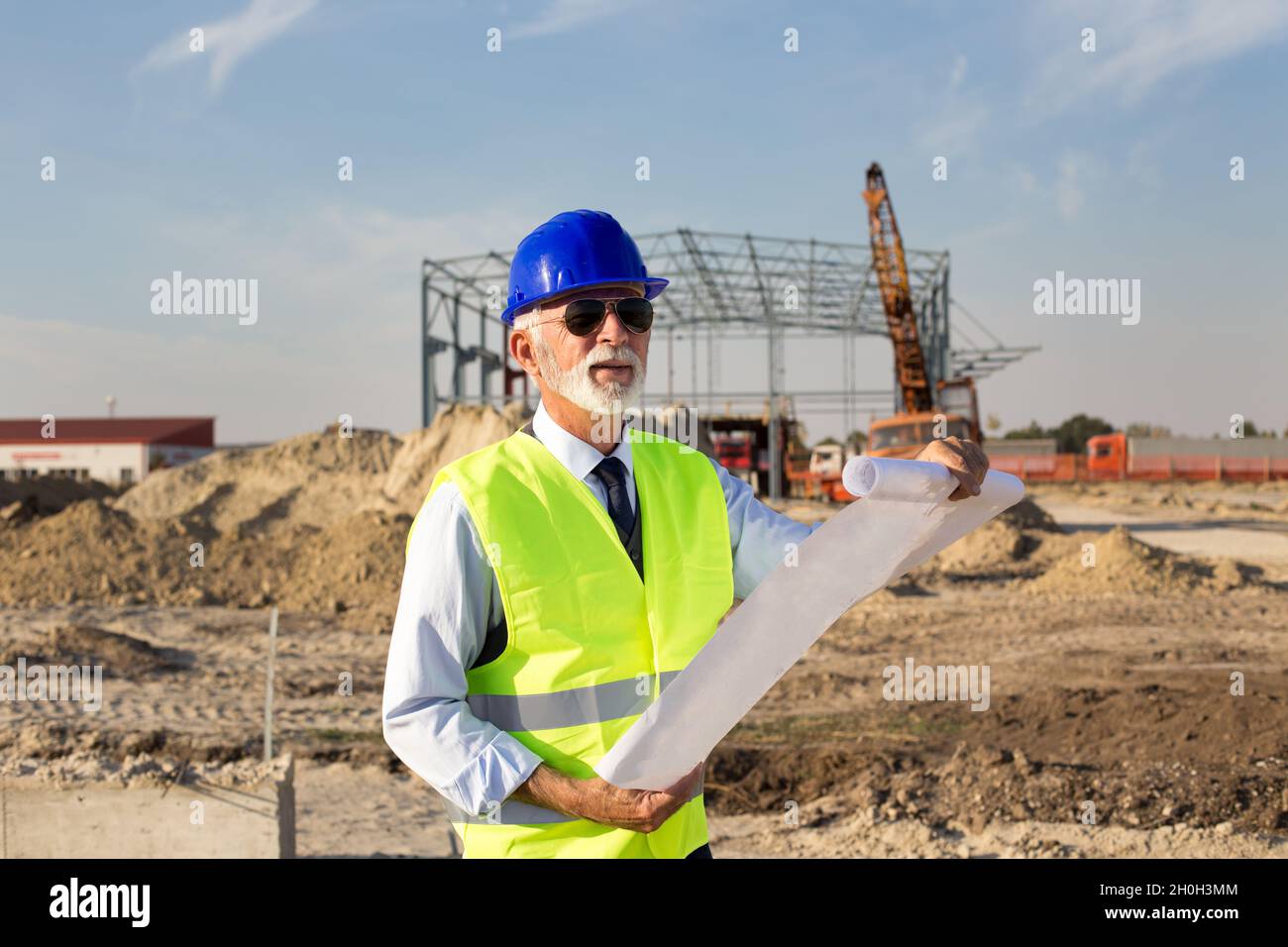 Senior engineer looking at blueprints in front of metal construction at building site Stock Photo