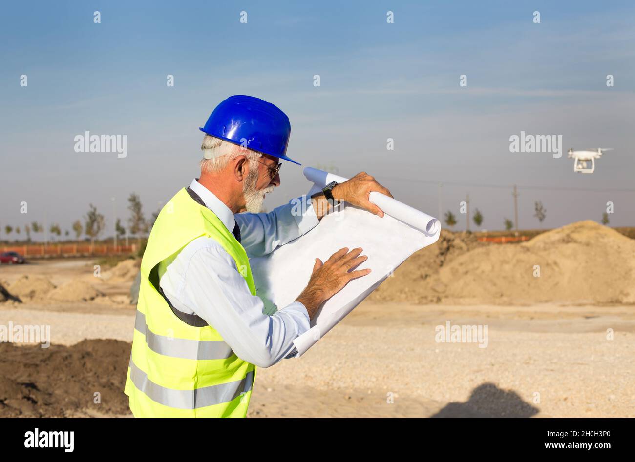 Senior engineer looking at blueprints in front of metal construction at building site Stock Photo