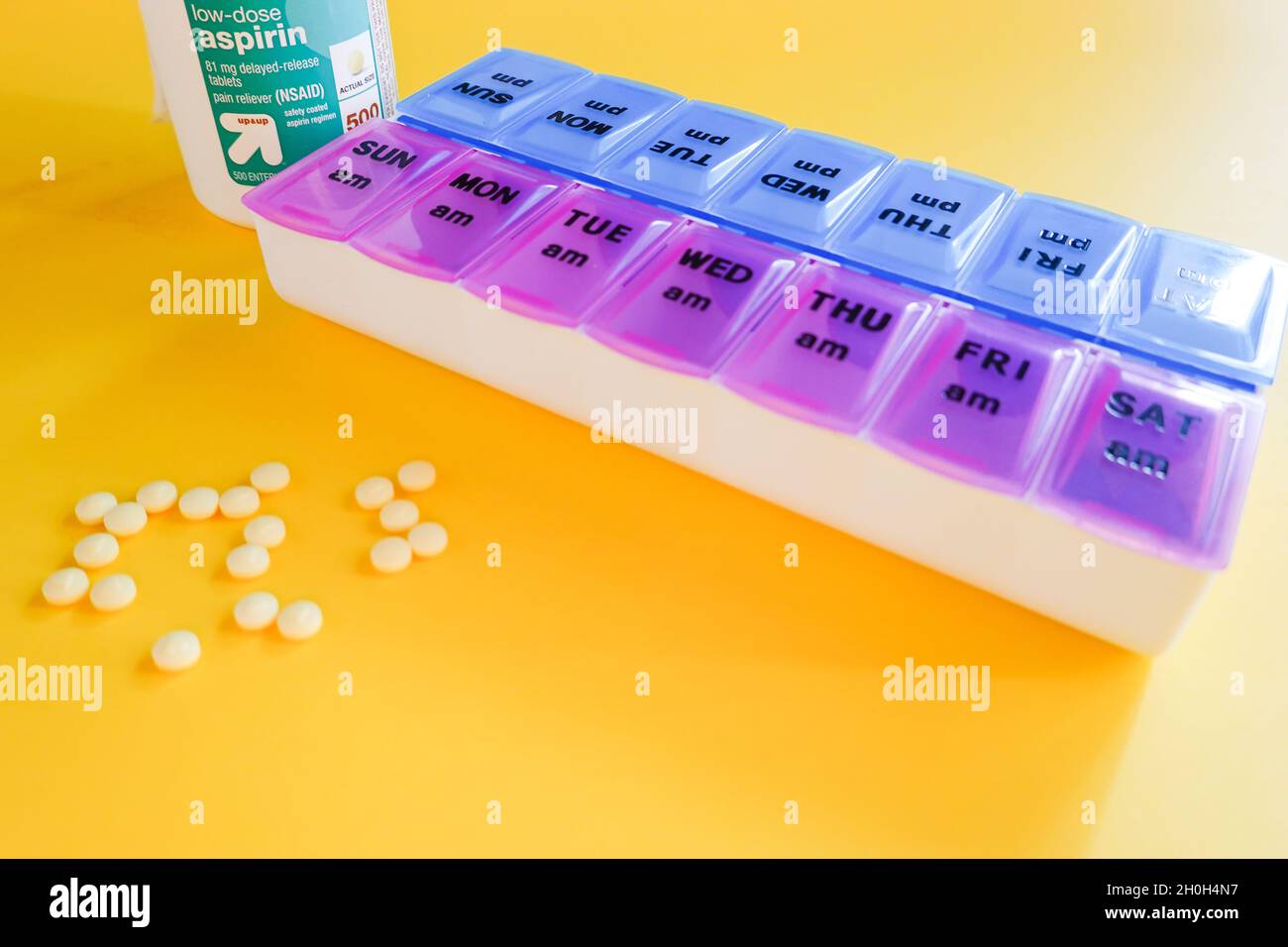 Bayer low dose safety coated 81 mg aspirin tablet container against a yellow background with a daily pill planner box Stock Photo