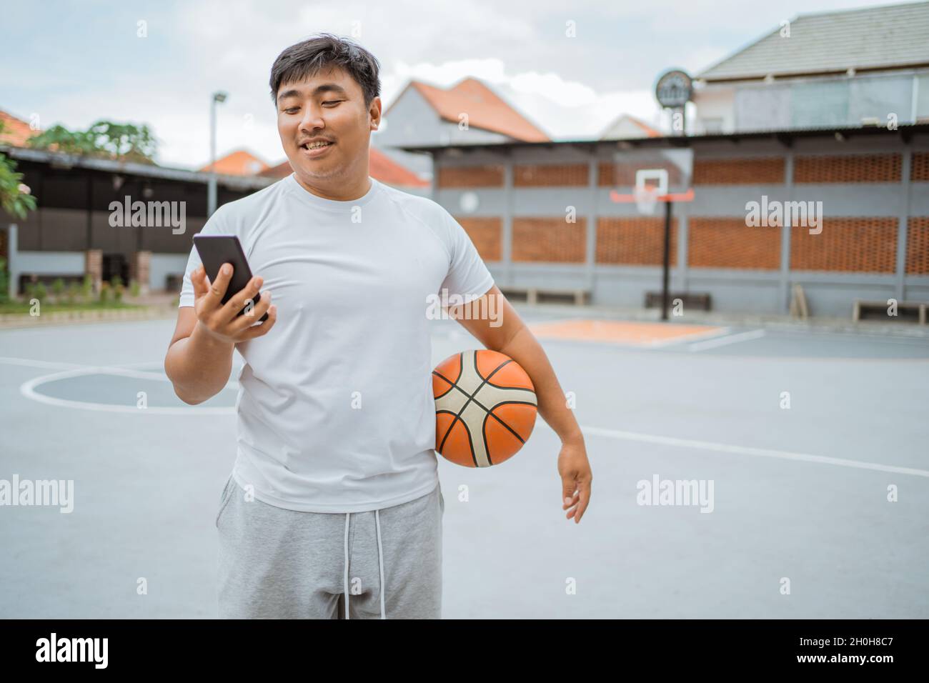 a basketball player using a mobile phone while standing holding the ball Stock Photo