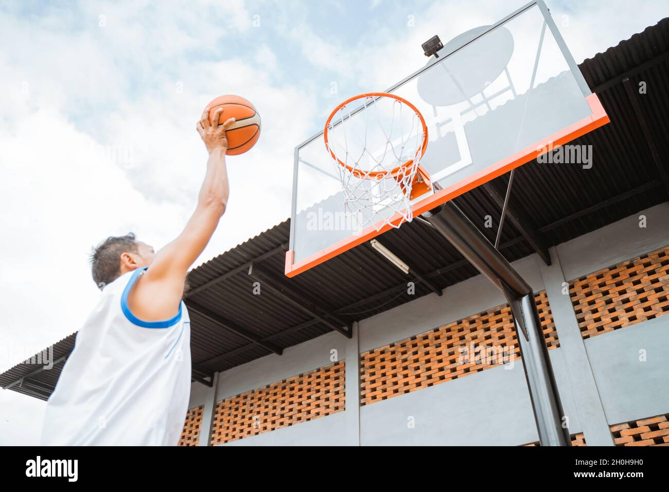 a basketball player holding a ball takes a lay up shot into the hoop Stock Photo