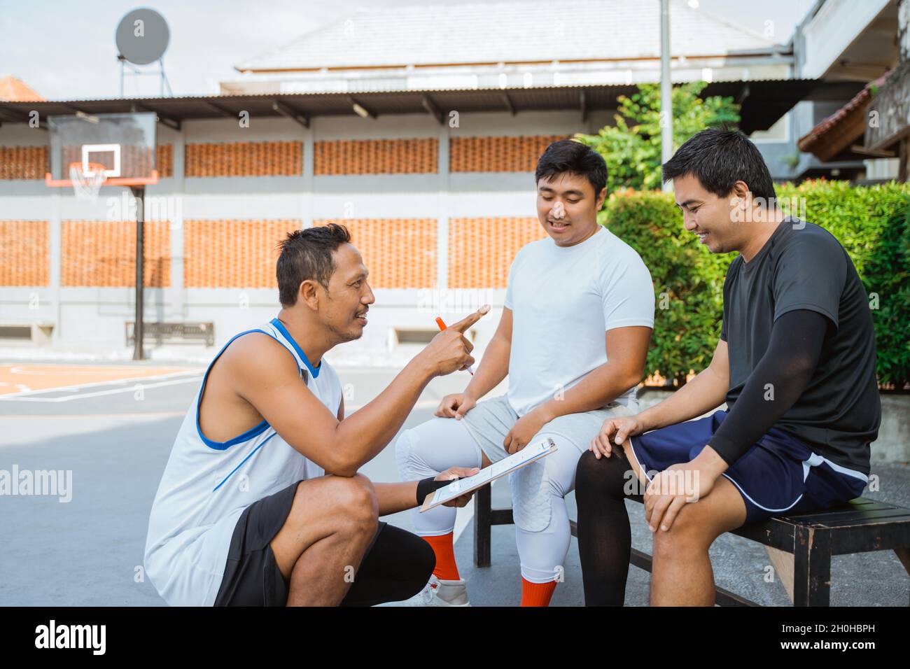 coach holding a clipboard giving instructions to two basketball players