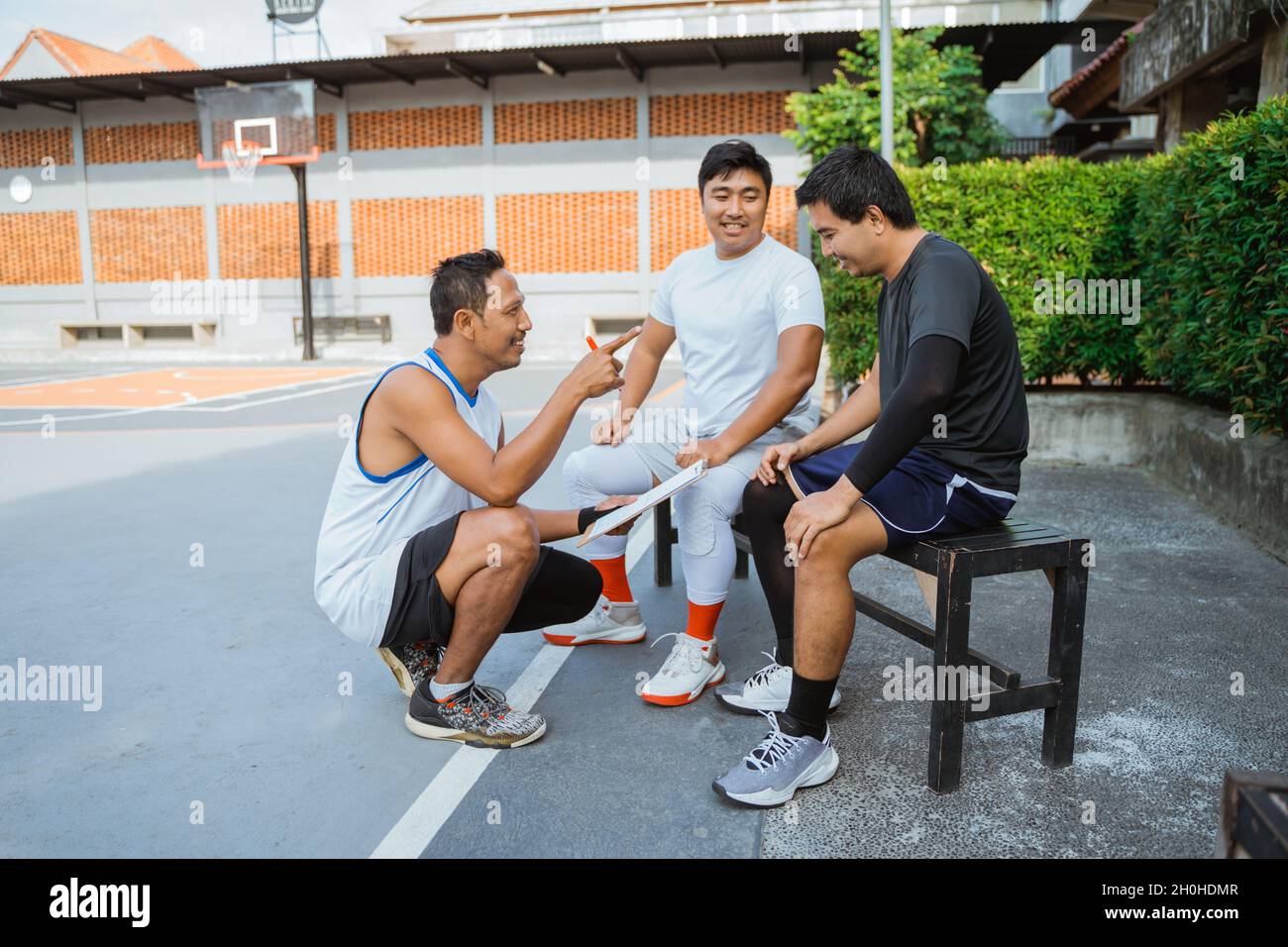 coach holding a clipboard giving instructions to two basketball players
