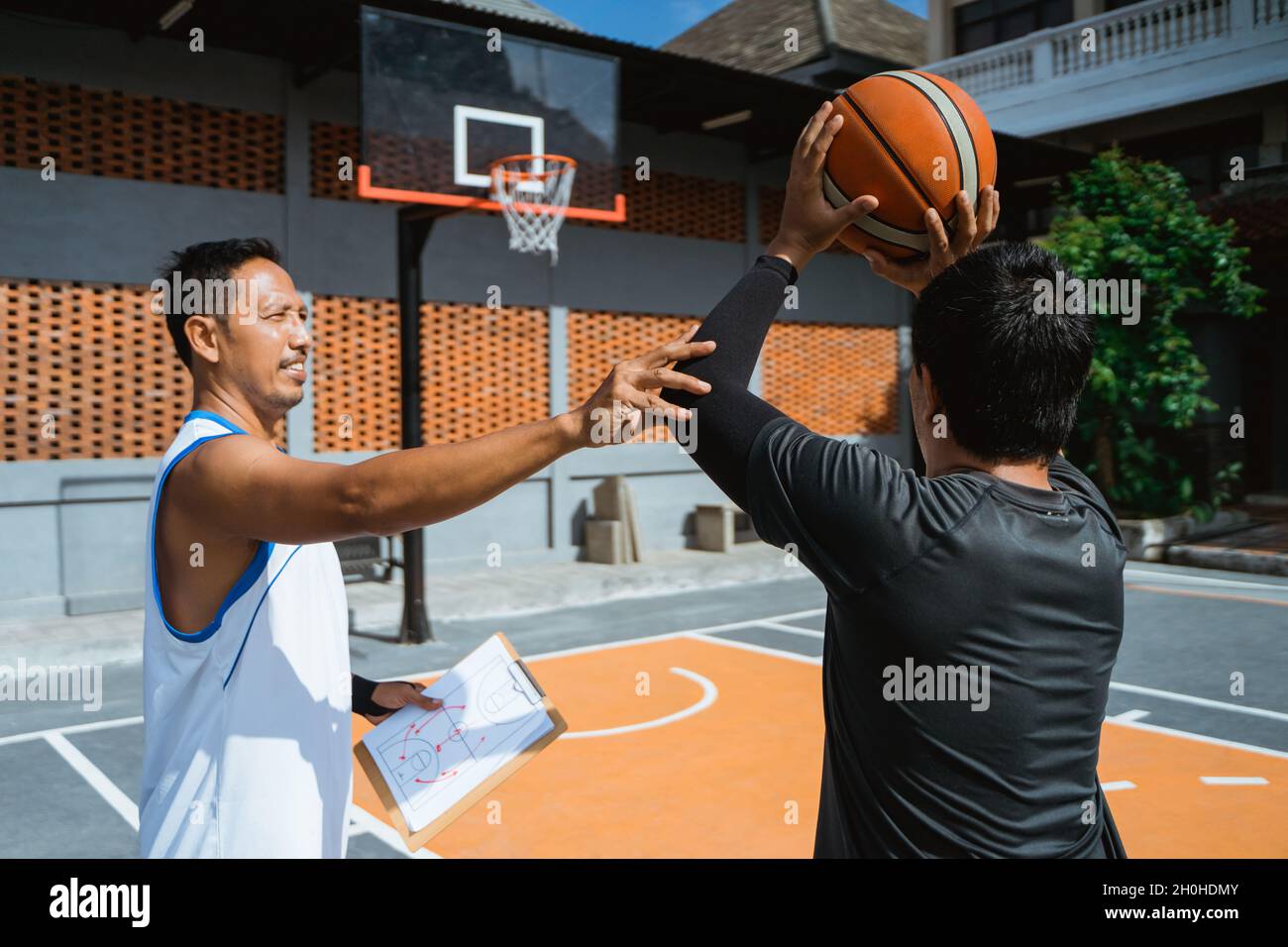 a coach advises a male basketball player to shoot the ball in the hoop Stock Photo