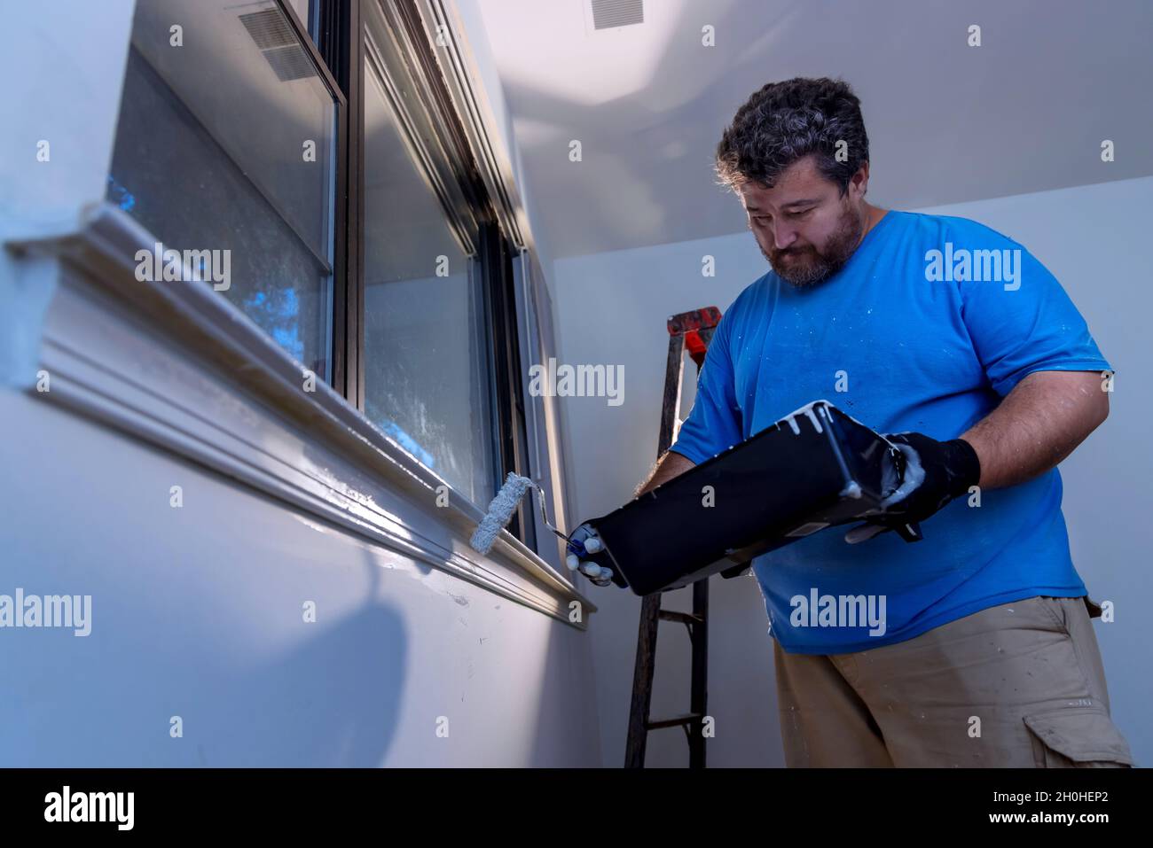 Worker painting using paint roller on layer white color a window frame