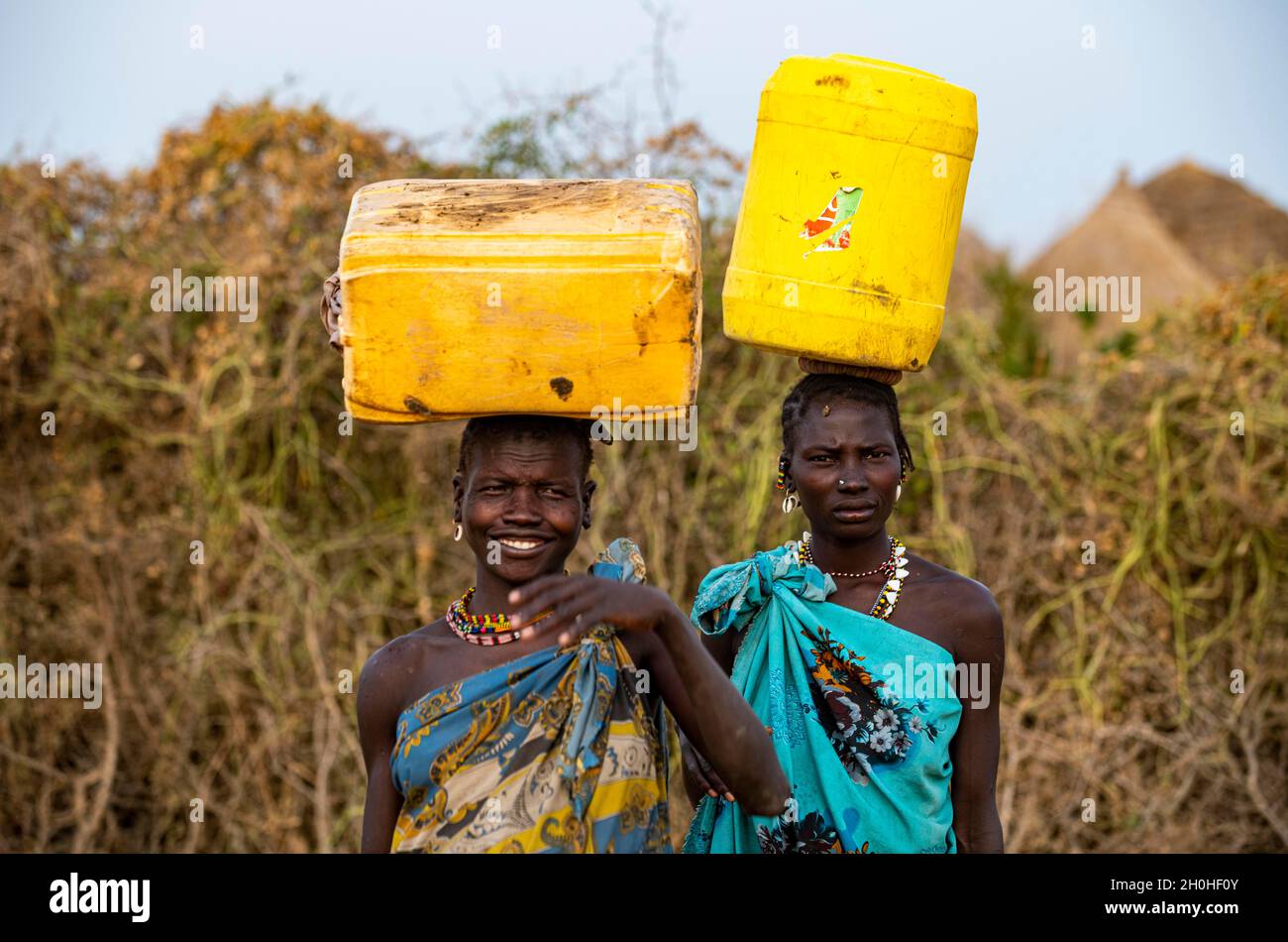 Traditional dressed women carrying water containers, Jiye tribe, Eastern Equatoria State, South Sudan Stock Photo