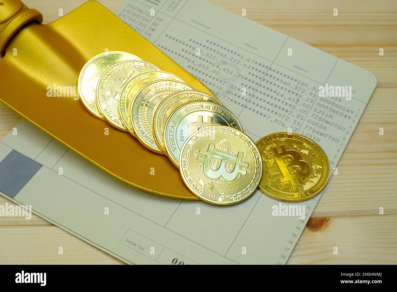 Close up of gold bitcoin coins on bank passbook with a golden shovel on wooden table Stock Photo