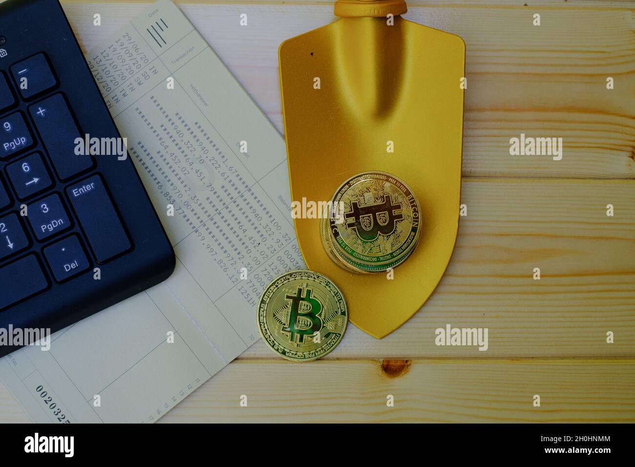 Close up of gold bitcoin coins on bank passbook with a golden shovel on wooden table Stock Photo