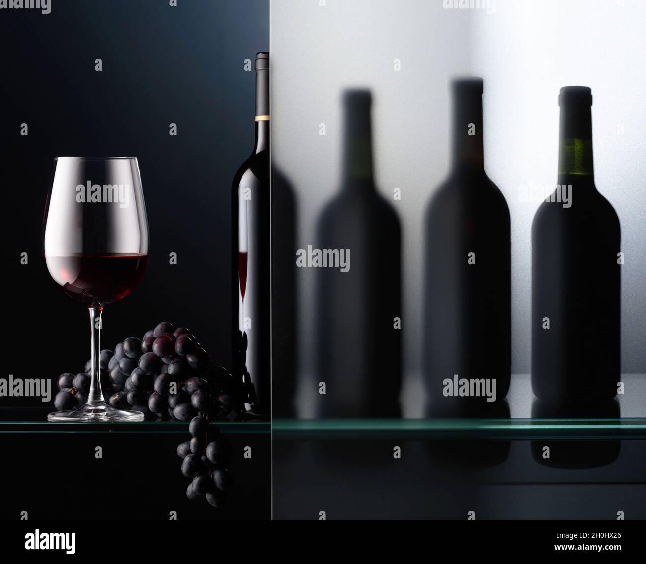 Bottles and a glass of red wine with a bunch of blue grapes. The still ...