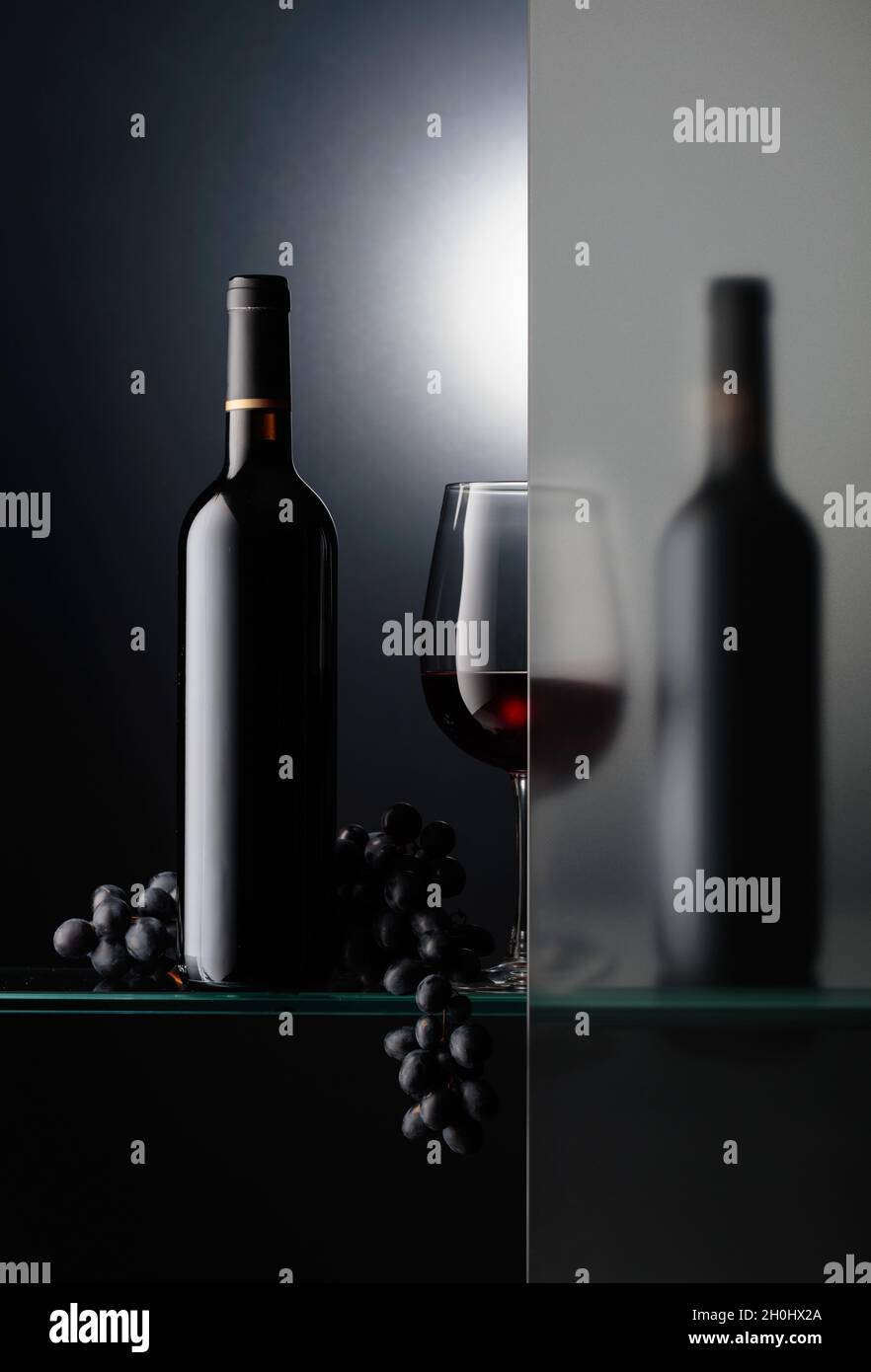 Bottles and a glass of red wine with a bunch of blue grapes. The still ...