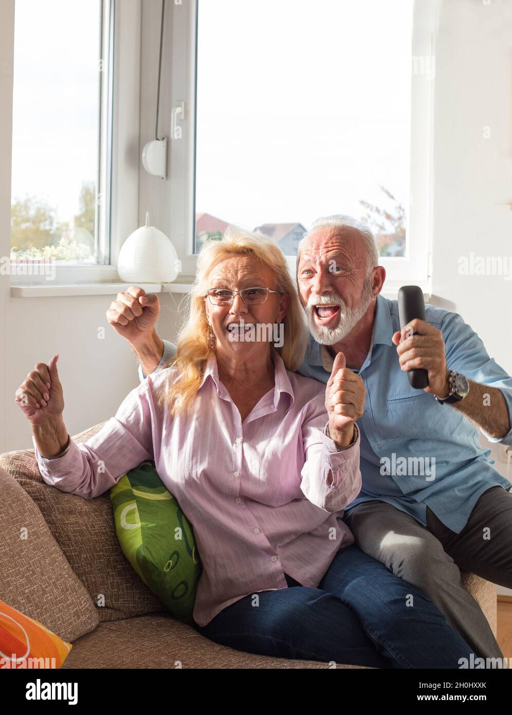 Excited elderly couple watching tv and cheering on sofa in living room Stock Photo