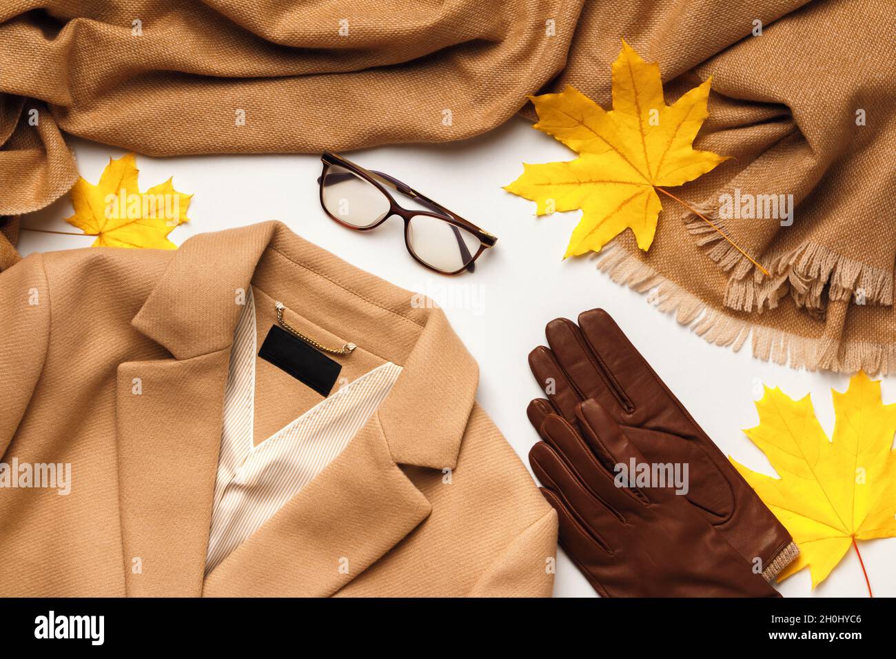 Warm autumn winter clothes. Coat scarf stole glasses gloves with yellow fallen maple leaves. Flat lay top view Stock Photo