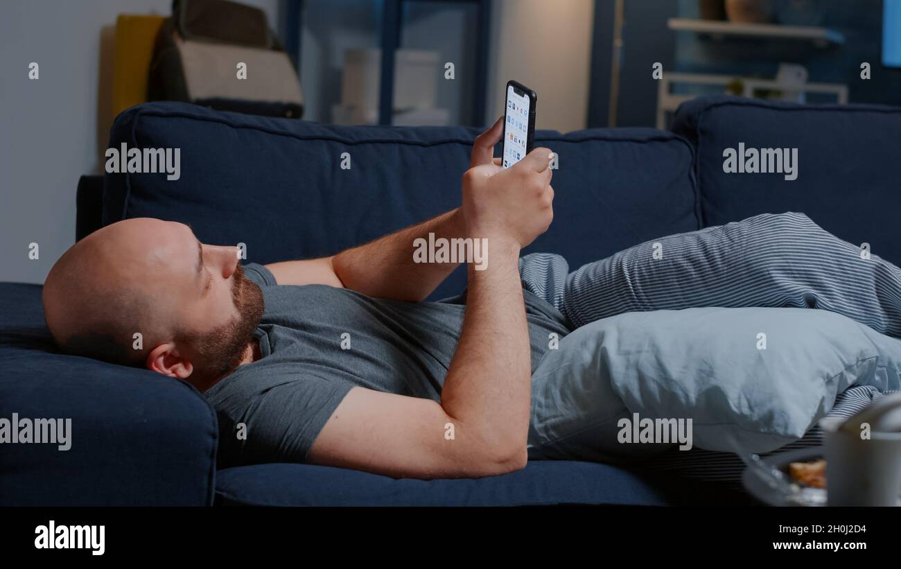 Upset man caused by break up lying on sofa at home browsing on