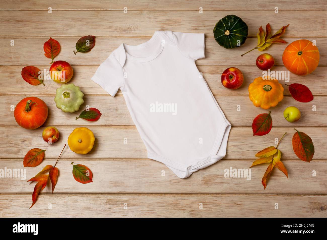 White cotton baby short sleeve onesie mockup with fall leaves, apples, yellow, red and green pumpkins. Design gender neutral bodysuit template, newbor Stock Photo