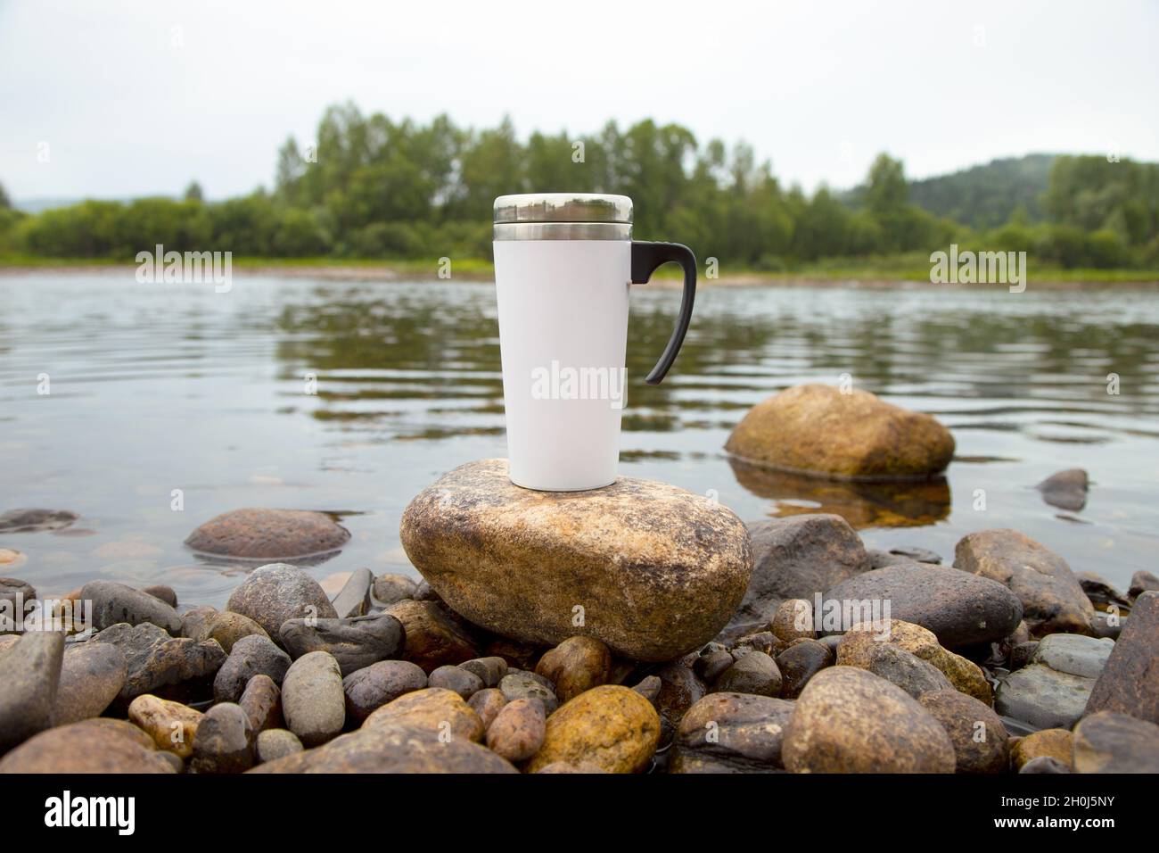 White travel coffee mug mockup with stony river bottom. Empty mug mock up for design promotion. Stock Photo